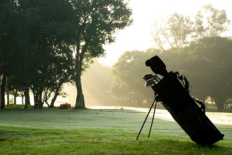 Photo of a golf bag standing silhouetted against a golf green.